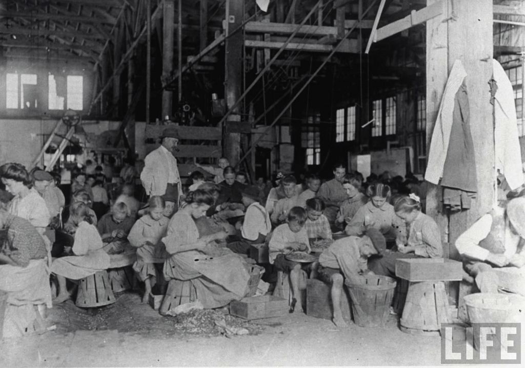 Child cannery workers sitting on bushelbaskets as they prepare beans under watchful eye of foreman. Source: LIFE Magazine